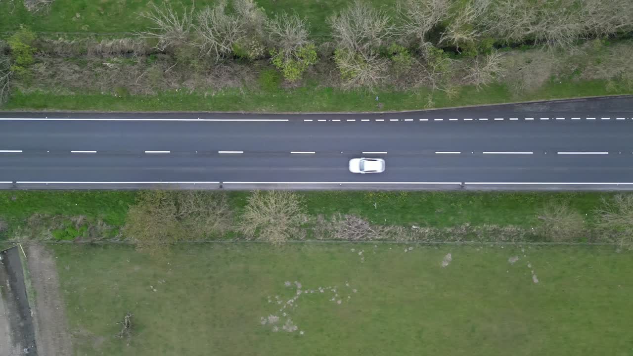Overhead drone view captures car cruising along highway, framed by lush green trees in England, UK. The straight road and vibrant foliage create stunning contrast in serene landscape