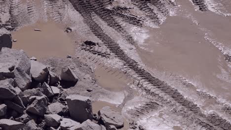 Tire-tracks-and-puddles-on-a-muddy-quarry-road-with-scattered-stones