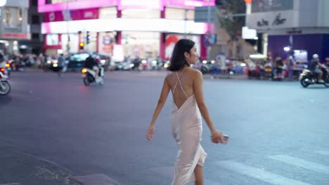 woman walking through a busy city night intersection in a dress