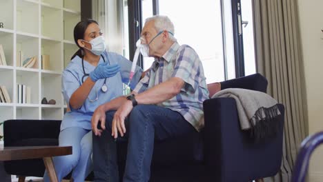 Video-of-biracial-female-doctor-in-face-mask-keeping-oxygen-to-caucasian-senior-man