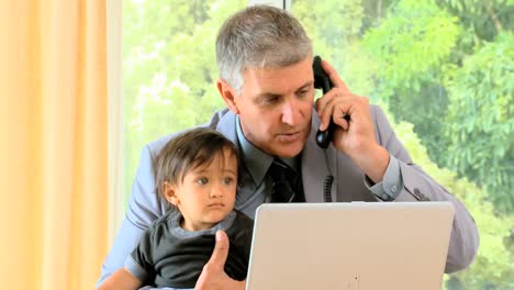 Man-talking-on-phone-while-his-baby-is-fidgeting-on-his-lap