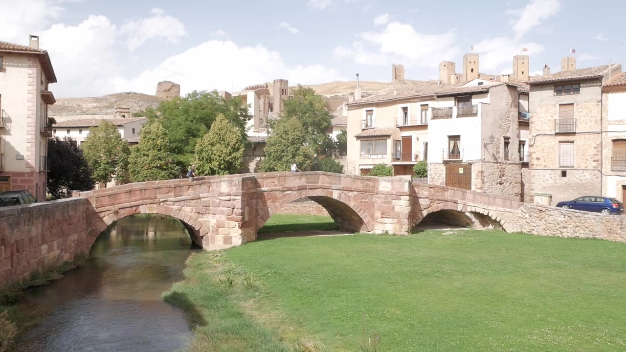 Puente de piedra histórico cruza el río en Molina de Aragón con vista al pueblo y al castillo.