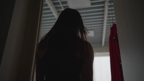 back view coach walking into exercise room with red hammocks hanging by window under soft natural light capturing movement and anticipation of upcoming fitness session with calm atmosphere