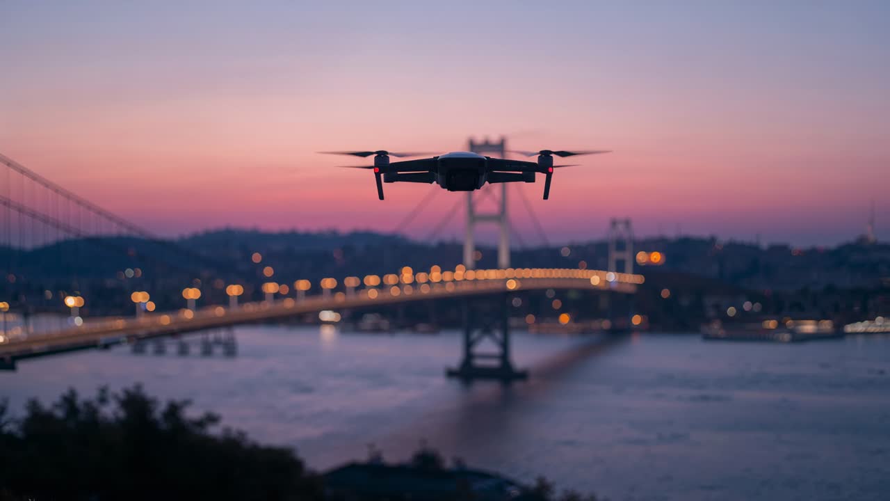Hovering quadcopter holding steady at dusk over water, propellers spinning, framing bridge lights