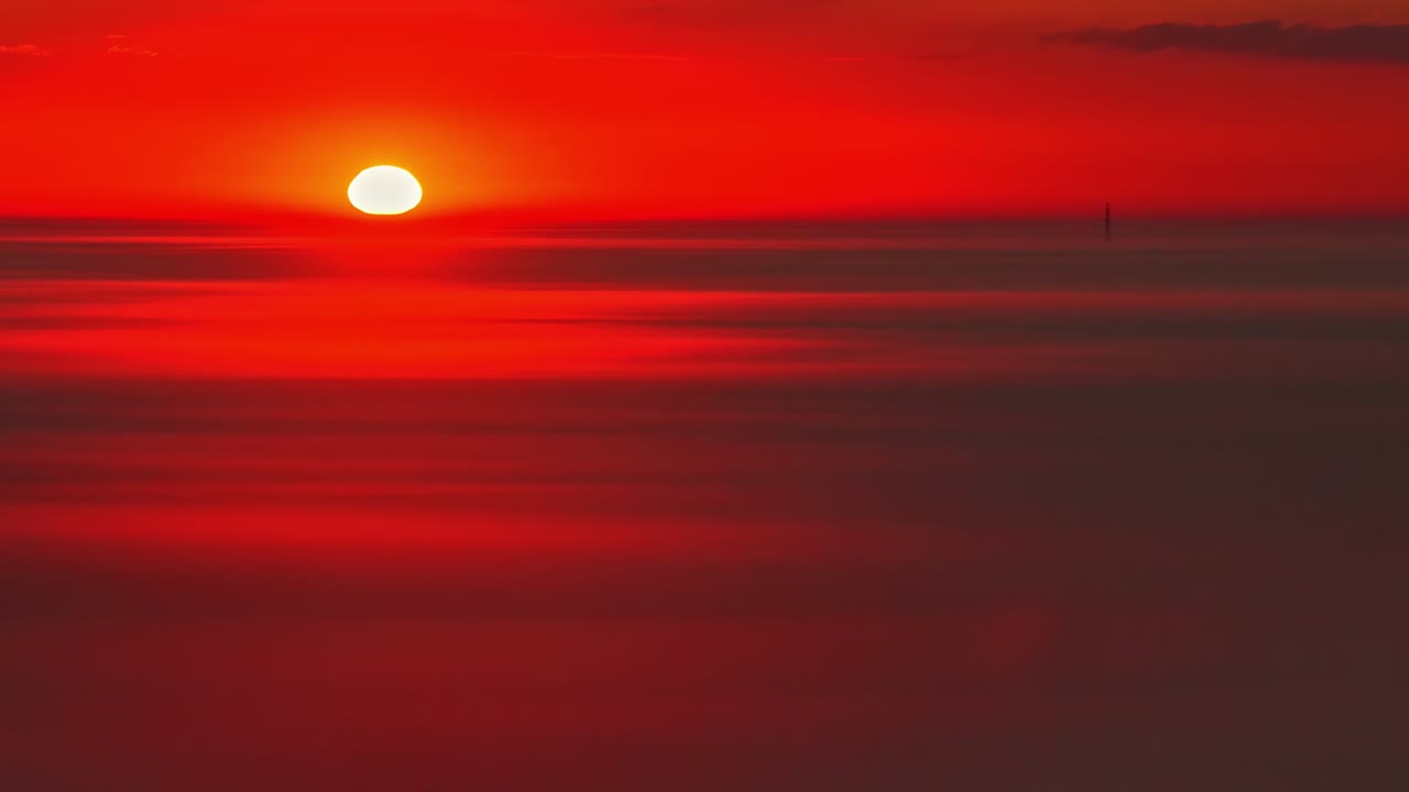Fiery red sunset casting light through thin horizontal cloud bands in the evening sky