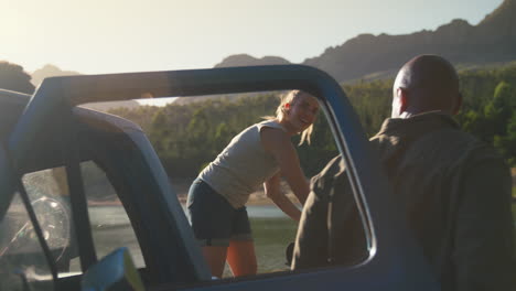 group of friends unloading backpacks from pick up truck on road trip by lake in countryside