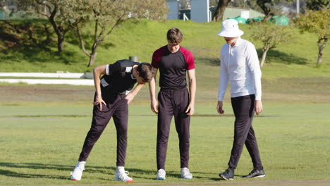 two multiracial male cricket players and male umpire throwing coin, shaking hands on pitch