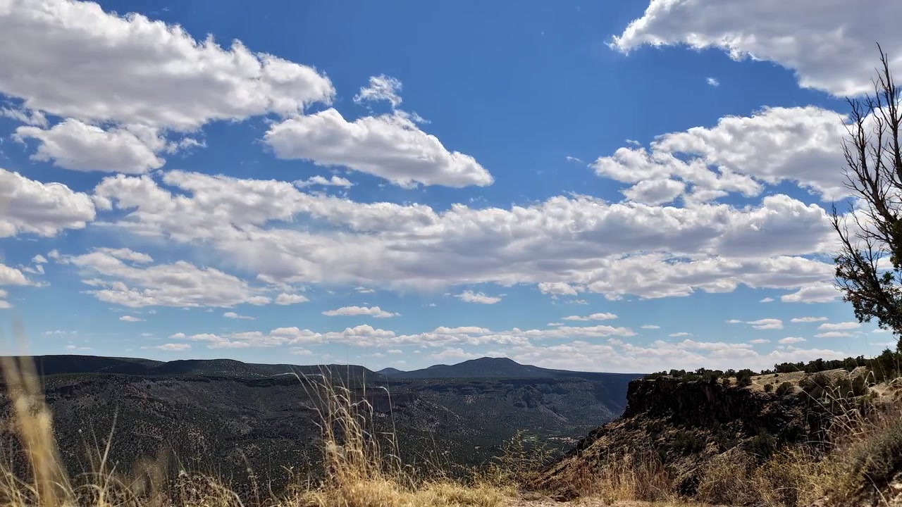 Timelapse 4K stabile cattura nuvole in rapido movimento sopra una montagna di canyon scoscesa. Il movimento atmosferico cinematografico rivela erba dorata mossa dal vento in primo piano in una veduta desertica del sud-ovest.