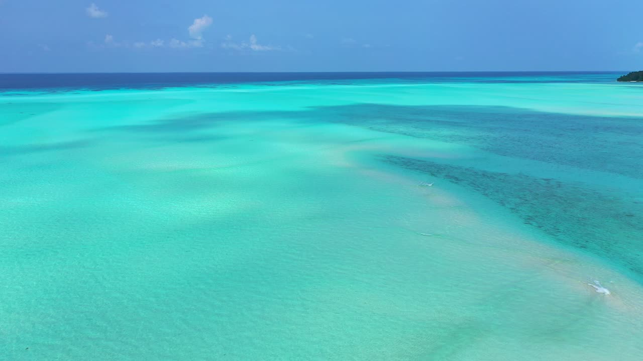 Texture del mare turchese con acqua calma e cristallina su un fondale sabbioso bianco delimitato dall'oceano blu profondo e dal cielo luminoso, Maldive