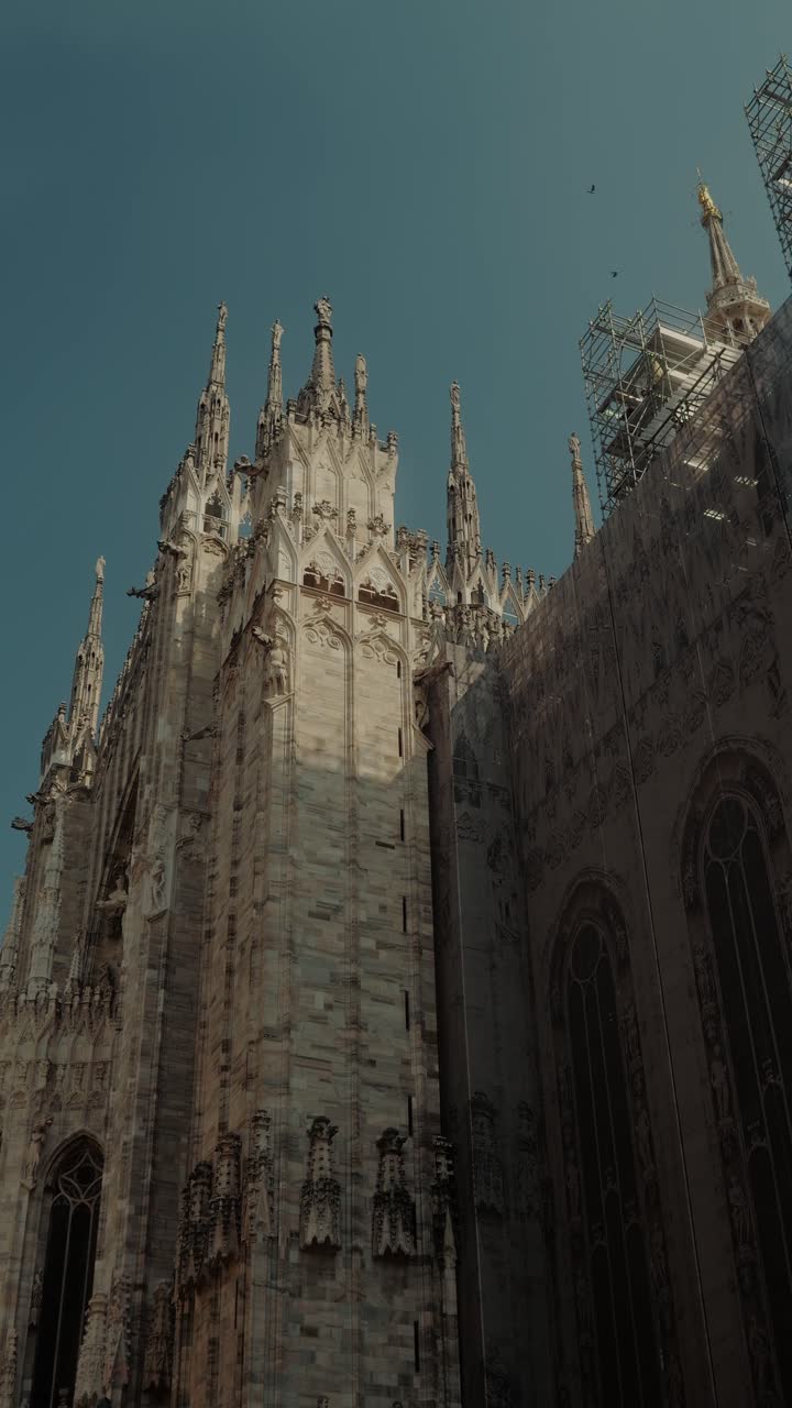 Vista laterale del Duomo di Milano, caratterizzato da guglie gotiche, dettagli in pietra e la scala monumentale di questo iconico punto di riferimento milanese.