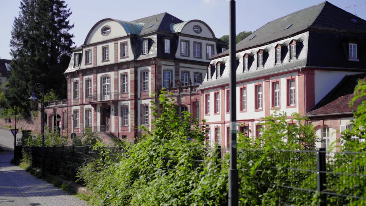 A slow-motion capture of the beautiful and historic Von der Leyen High School in Blieskastel, Germany. Surrounded by lush greenery, the classic architecture shines in the warm summer sun.