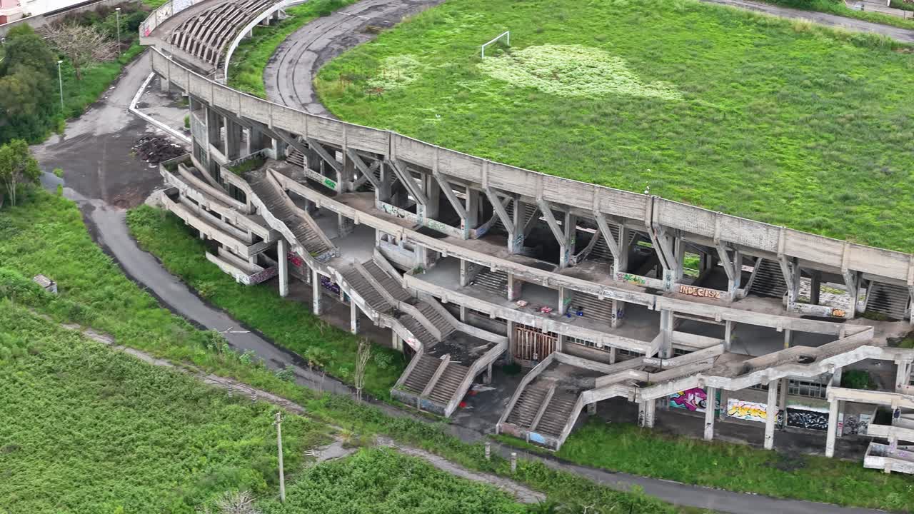 Drone telephoto overview of backside of abandoned stadium, empty grassy infield