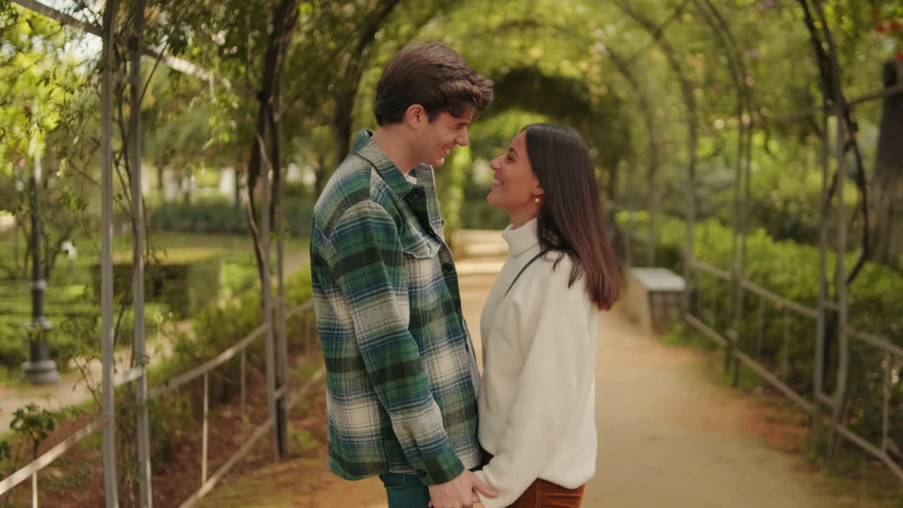 Happy young young pair man and woman standing holding hands against green arch