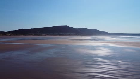 sun reflecting on surface water on rhossili bay beach with moorland background. aerial, drone view footage 4k
