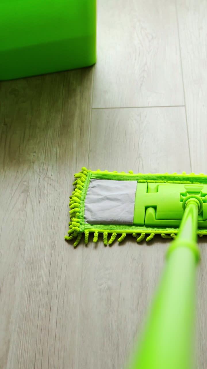 Cleaning floor with water and swab. Green mop moving on the parquet floor near the green bucket with water. Daily household routine. Hygiene concept. Vertical video