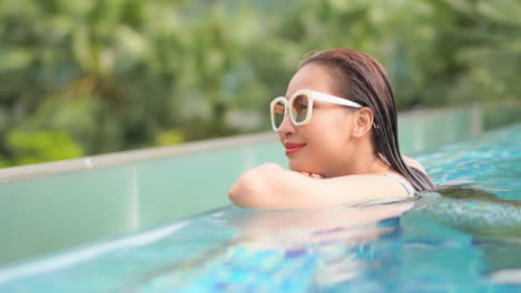 Primer-Plano-De-Mujer-Asiática-Con-Gafas-De-Sol-Relajándose-En-La-Piscina-Sola