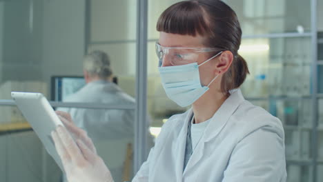 masked female scientist using tablet in lab