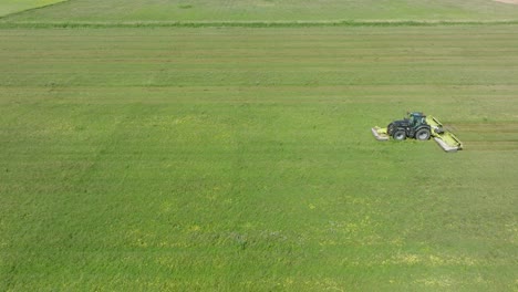 aerial establishing view of a tractor mowing a fresh green grass field, a farmer in a modern tractor preparing food for farm animals, sunny summer day, wide drone dolly shot moving left