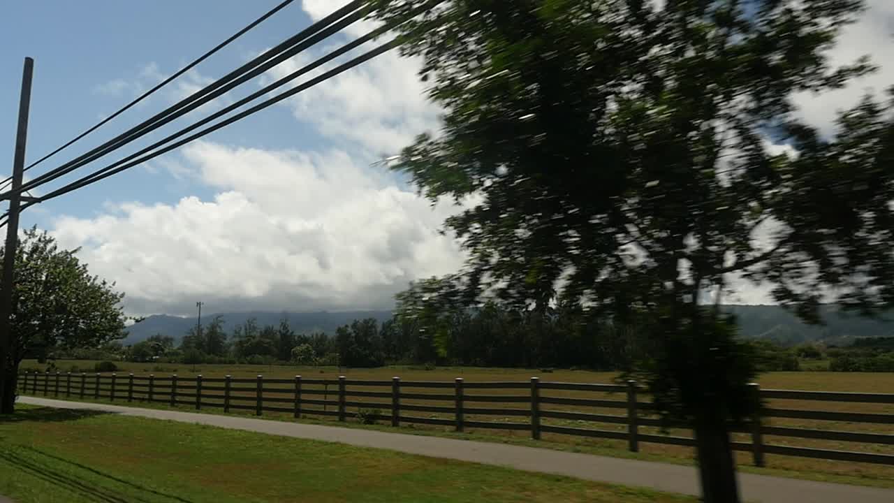 una toma en movimiento del límite de un rancho de oahu con vallas y postes de telégrafo con nubes blancas esponjosas y montañas en la costa norte