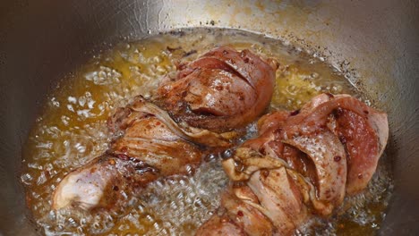 sizzling oil frying two pieces of chicken to golden brown in a stainless steel pan