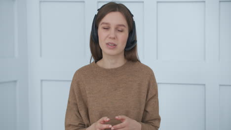 mujer encantadora con auriculares está saludando por videollamada mirando a la cámara sentada en la habitación retrato medio