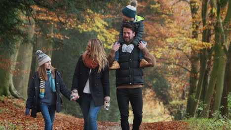 smiling family walking along path through autumn countryside as father carries son on shoulders