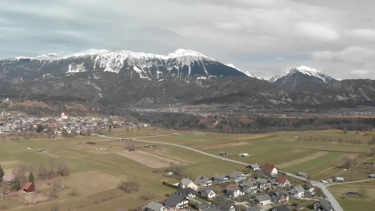 Aerial view of a little old alpine village at the bottom of the Alps mountains with snow peaks and cloudy cold day