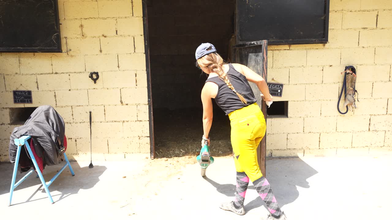 Female keeper uses a blower to push straw and dust into stalls while cleaning the stables exterior