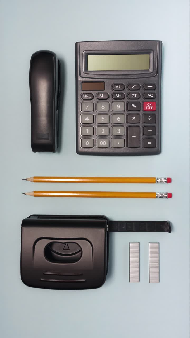 Looping vertical stop motion arranging calculator, stapler, pencils, hole punch and staples on a light blue desk