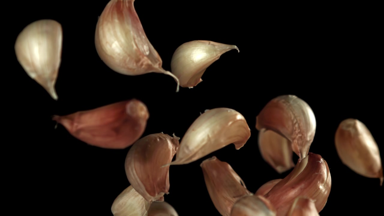 Spicchi d'aglio freschi che cadono al rallentatore su sfondo nero
