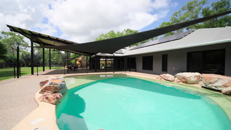 luxury elegant tropical home on large rural estate with artistic pool surrounded by rock boulder features under sun shade in backyard