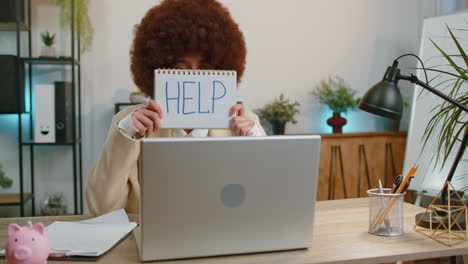 Overworked-tired-freelance-businesswoman-works-on-laptop-showing-inscription-notebook-with-Help-text