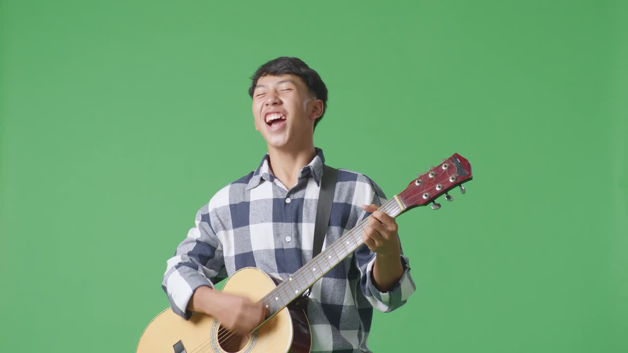 젊은 아시아 십대 소년이 녹색 화면 배경에서 록 음악과 함께 기타를 연주하고 있습니다.