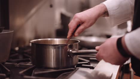 cook scoops through a saucepan with a spatula while steam comes from a frying pan in the background