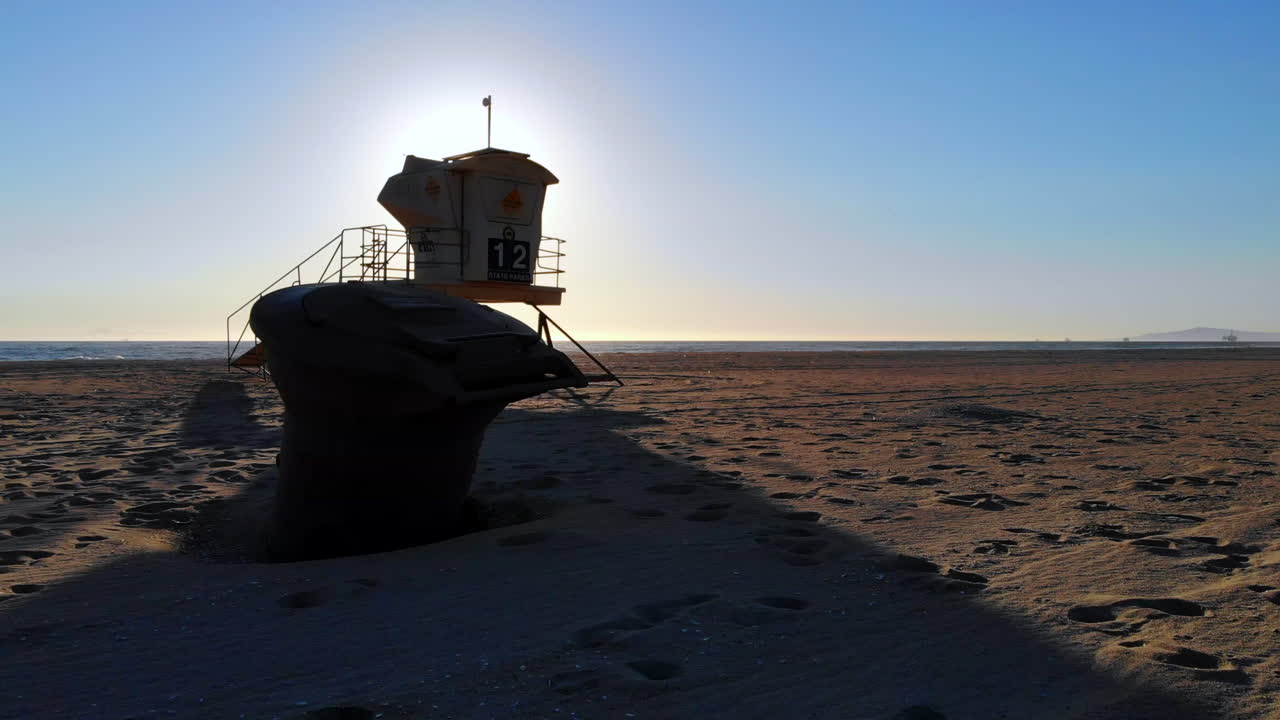 인명 구조원 탑과 쓰레기통 주변을 낮고 빠르게 날아다니며 공중 4k 드론으로 캘리포니아 헌팅턴 해변의 아름다운 파도와 일몰을 볼 수 있습니다.