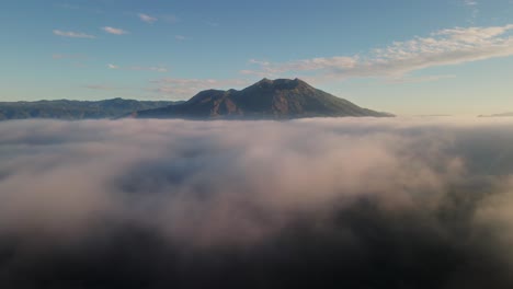 Aerial-tracking-shot-low-over-valley-covered-in-fog-with-mountain-background