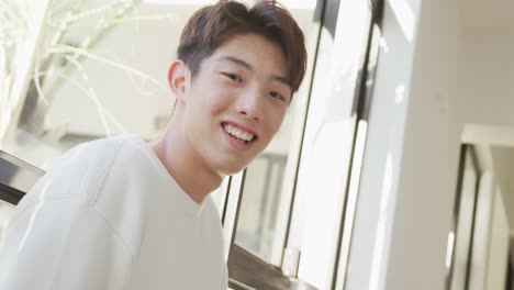 portrait of happy asian male teenager leaning on window in living room