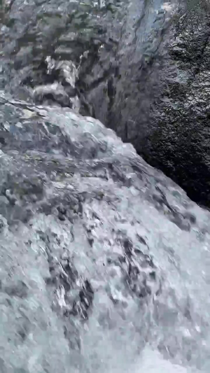 Primo piano dell'acqua che scorre su rocce scure in un ruscello