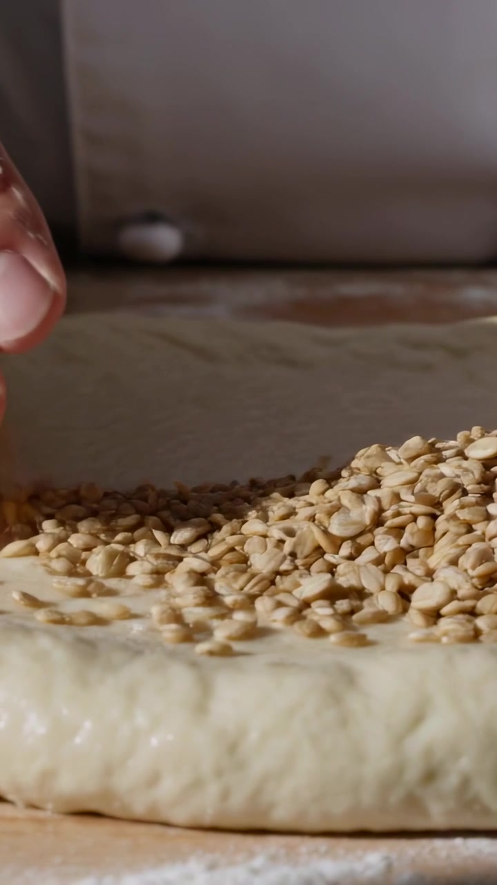 Video verticale: Entrando, la mano dello chef che sparge semi sull'impasto in una panetteria, con polsino e anello d'oro per la cottura