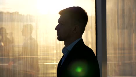 Young wealthy businessman in stylish suit walking through glass hall of modern office build. Profile of successful man going to home after hard working day. Handsome guy stepping indoor. Slow motion