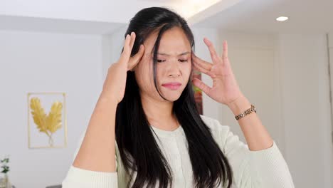 a woman appears distressed, holding her head in a well-lit room with minimal decor
