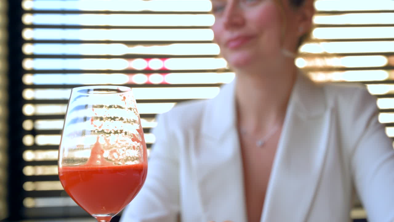 Frau mit weißem Blazer, die in einem Restaurant einen Karottensaft trinkt