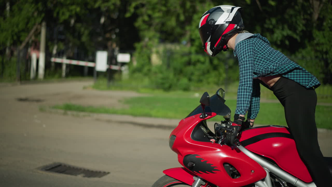 은 파워 자전거를 타고 헬을 착용 한 여자의 측면 뷰, 그녀는 일어서서 자전거에 다시 앉았을 때, 그녀의 셔츠는 바람에 날아다니며 밝은 빛 날에 그녀의 등 일부를 드러니다.