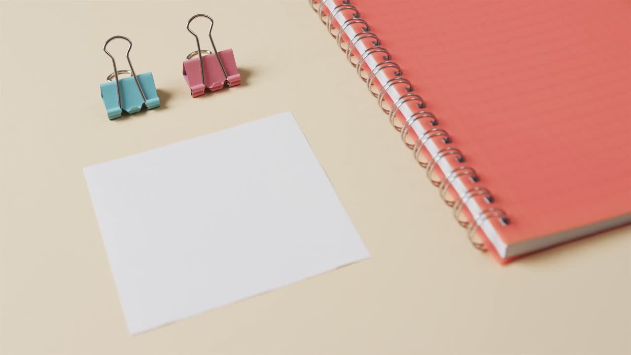 primer plano de un cuaderno rojo y artículos escolares dispuestos sobre un fondo beige, en cámara lenta