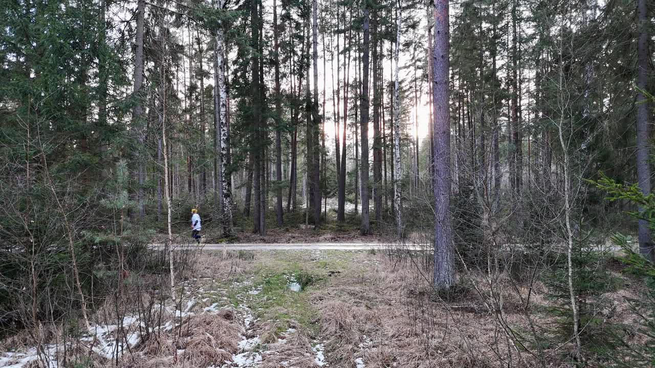 A runner in the woods in winter. Sun setting in the background. Drone.