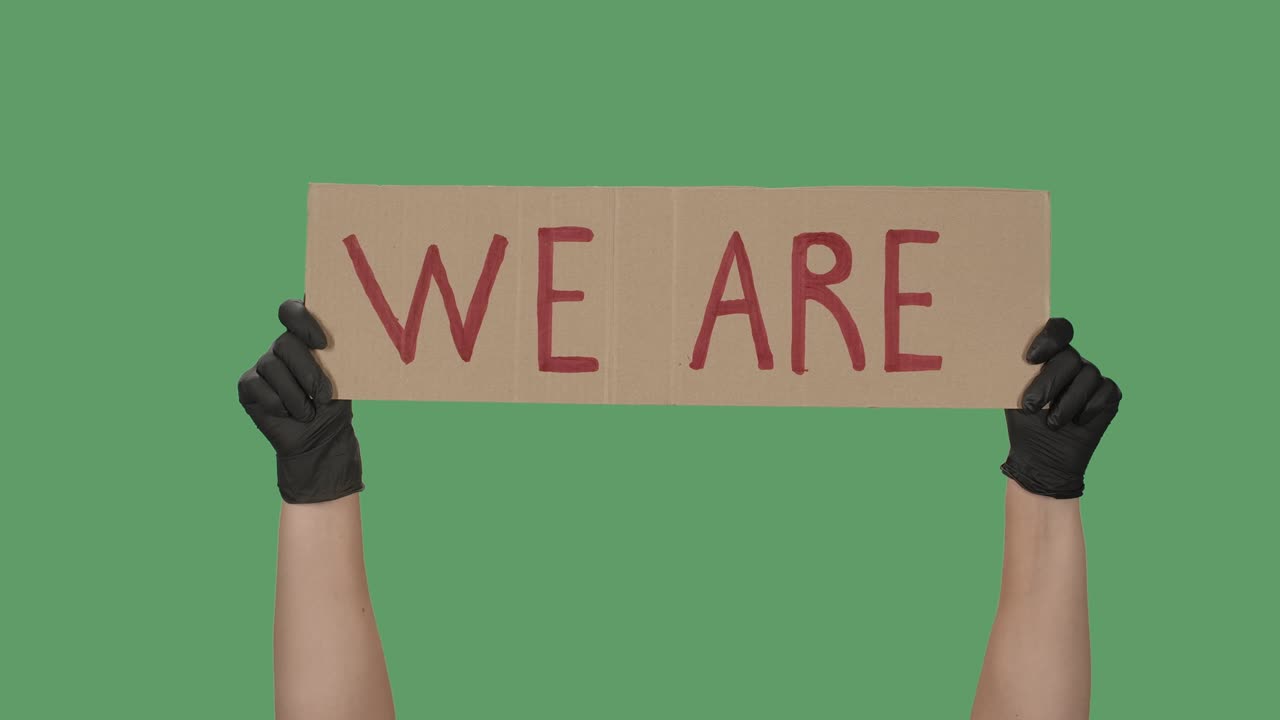 우리는 녹색 화면, 크로마 키의 배경에 있습니다. 검은 장갑을 입은 손은 카드보드 상자에서 포스터를 들고 있습니다. 시위는 평화적인 시위입니다.