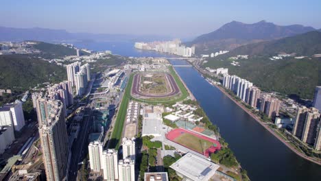 tall ultra-modern apartments with expansive shadows next to sha tin race track and the shing mun river on a hot summer day in hong kong