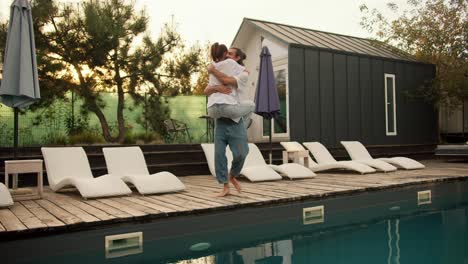 a girl jumps on her boyfriend and hugs him near the sunbeds by the pool. rest in the country house