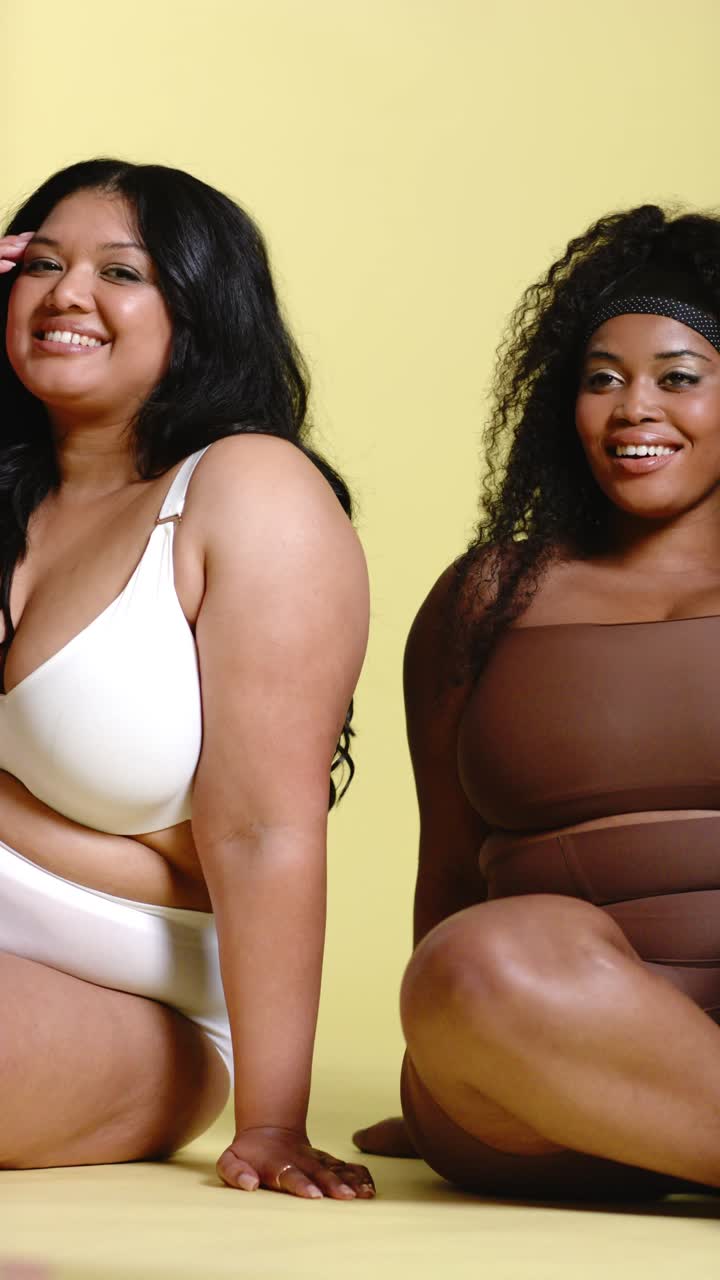 Video verticale: Amiche diverse che posano in intimo sedute in studio, spostando lo sguardo e sorridendo.