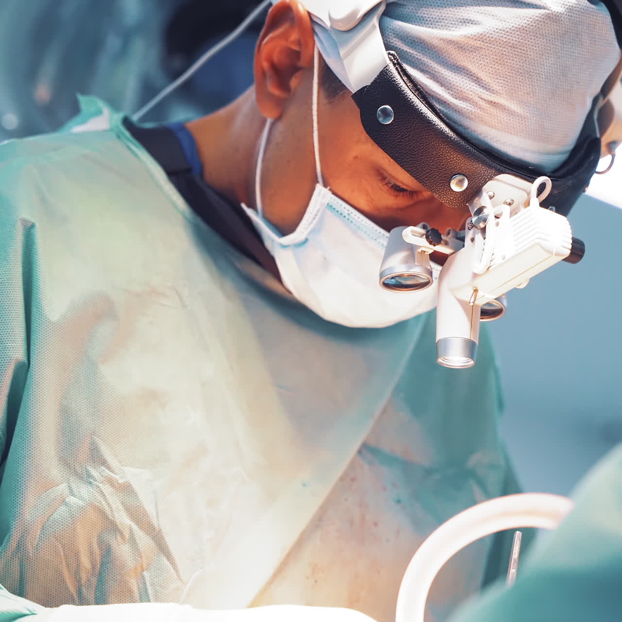 Male doctor in a medical mask and in protective uniform is doing operation. Surgeon's face with magnifying glasses is working in the operating room.
